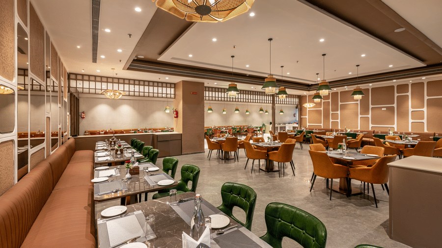 A modern dining area of the Blue Coriander restaurant featuring emerald green and orange armchairs, wooden tables, and elegant decor – Skkylight Lords Inn, Nanded