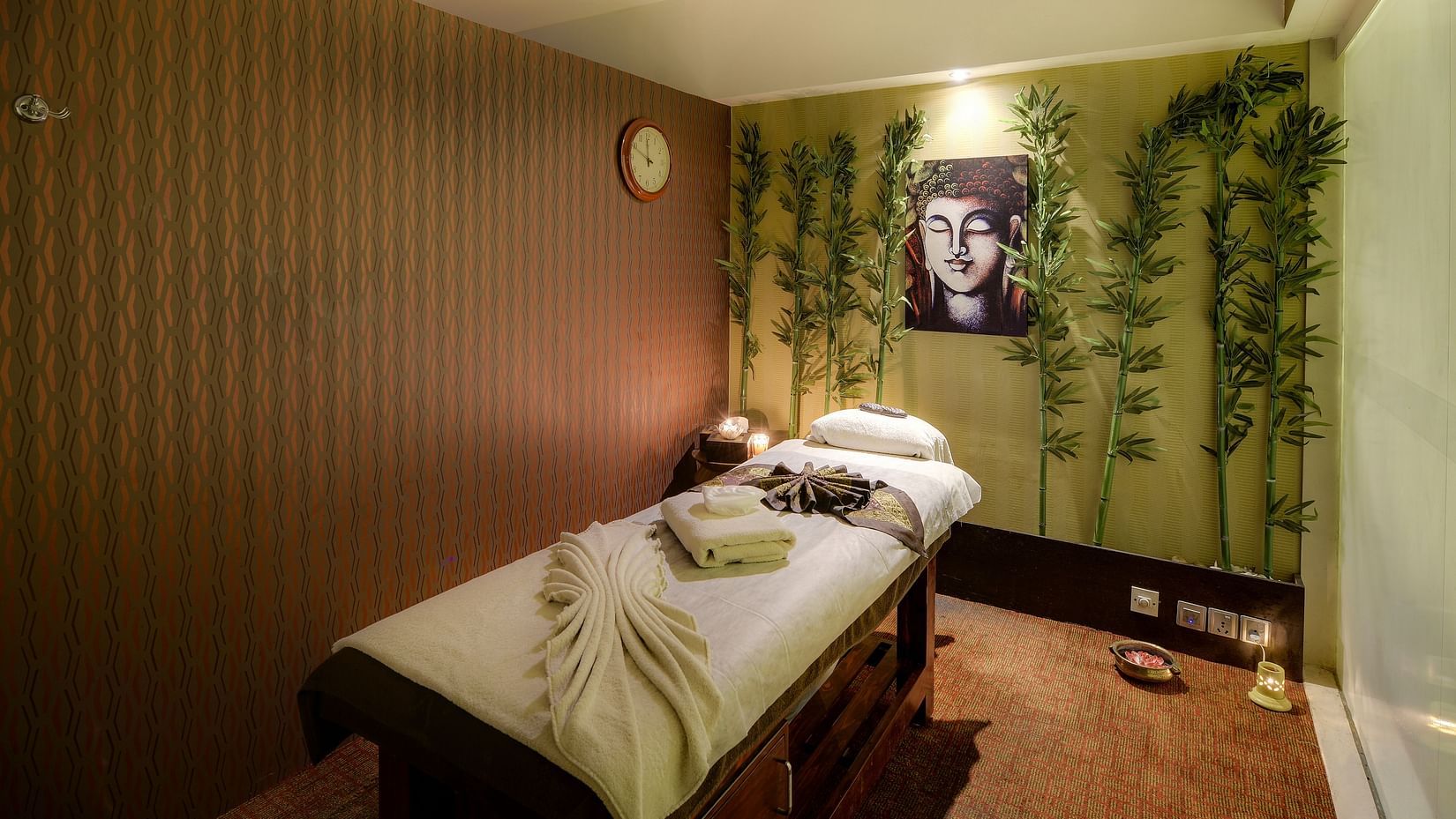 Image of a massage bed with towels on it and a photo of Lord Buddha on the wall behind it with artificial creepers hanging on the wall at Pride Hotel Bangalore