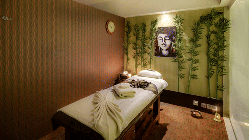 Image of a massage bed with towels on it and a photo of Lord Buddha on the wall behind it with artificial creepers hanging on the wall at Pride Premier Bengaluru