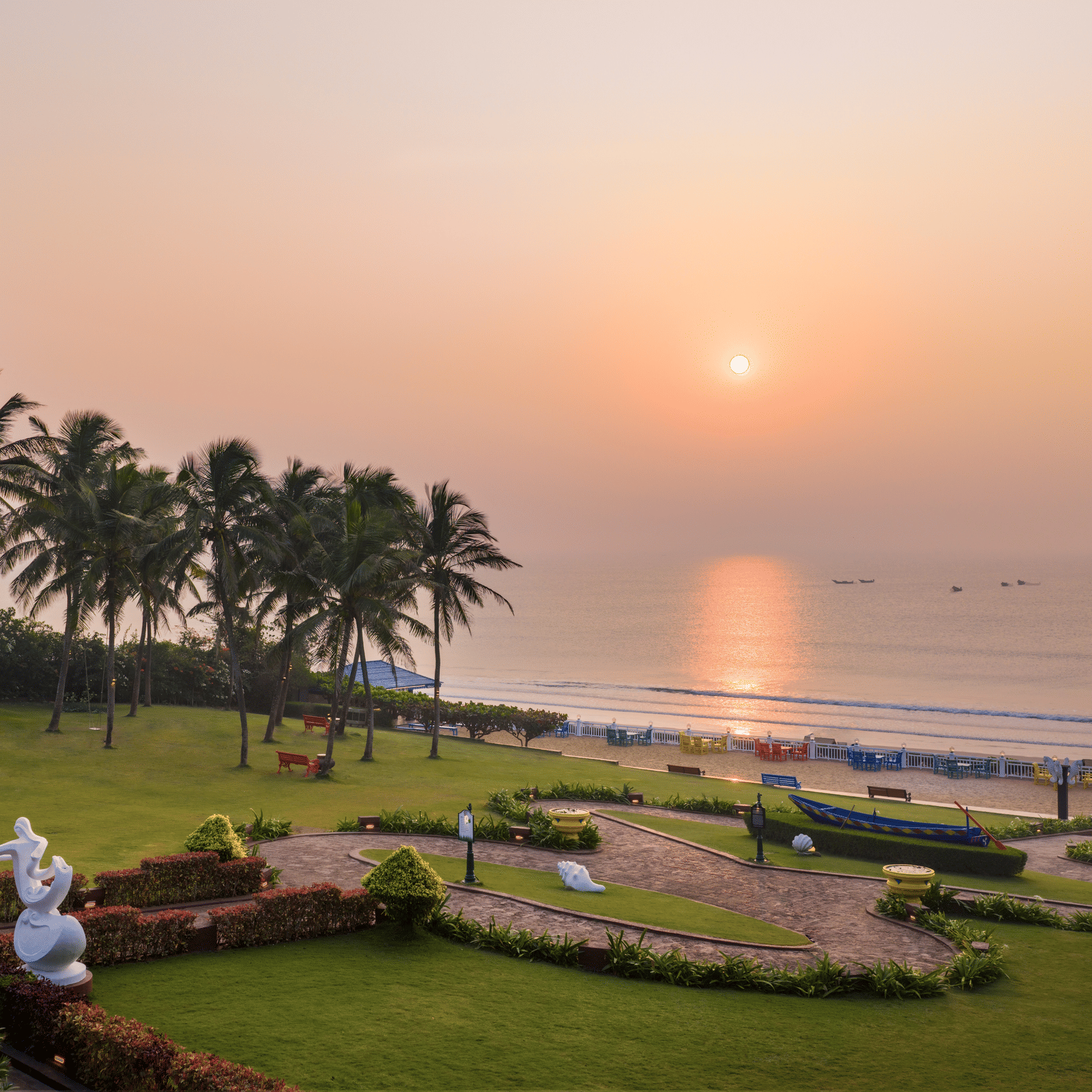 Elevated scene of gardens with sculptures and pathways leading to the beach and sea at sunset at MAYFAIR Palm Beach Resort, Gopalpur-on-Sea.