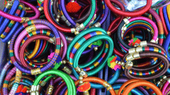  A vibrant pile of colourful bangles, wrapped in red, green, purple, and blue threads, with small pom-poms attached to some.