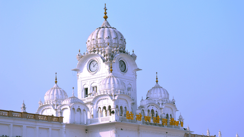 A close-up view of a white temple with multiple domes and a clock tower, under a clear blue sky.