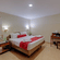 A spacious bedroom at Holiday Home Resort, Kodaikanal, featuring a neatly-made bed, a workspace with a table and a chair, a wall-mounted television, and a wooden dressing table. 