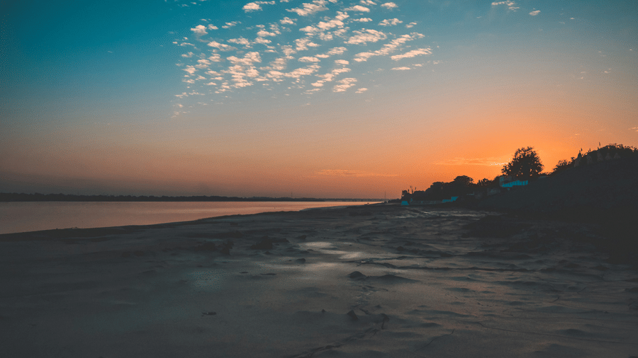 An overview of a beach in Bharuch during the sunset with orange-blue sky, white clouds, and the Arabian Sea in view. This is the mid-stop on your Narmada Parikrama by Bus tour.