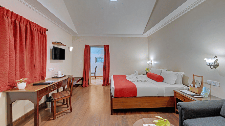 A bedroom at Holiday Home Resort, Kodaikanal, featuring a bed,  a wooden desk and a chair, and a sofa with a coffee table in the foreground. 