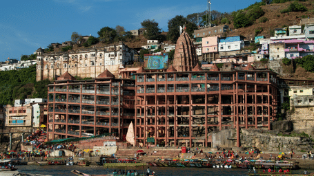 A hillside town with dense buildings overlooking a river, with greenery on the slopes above.