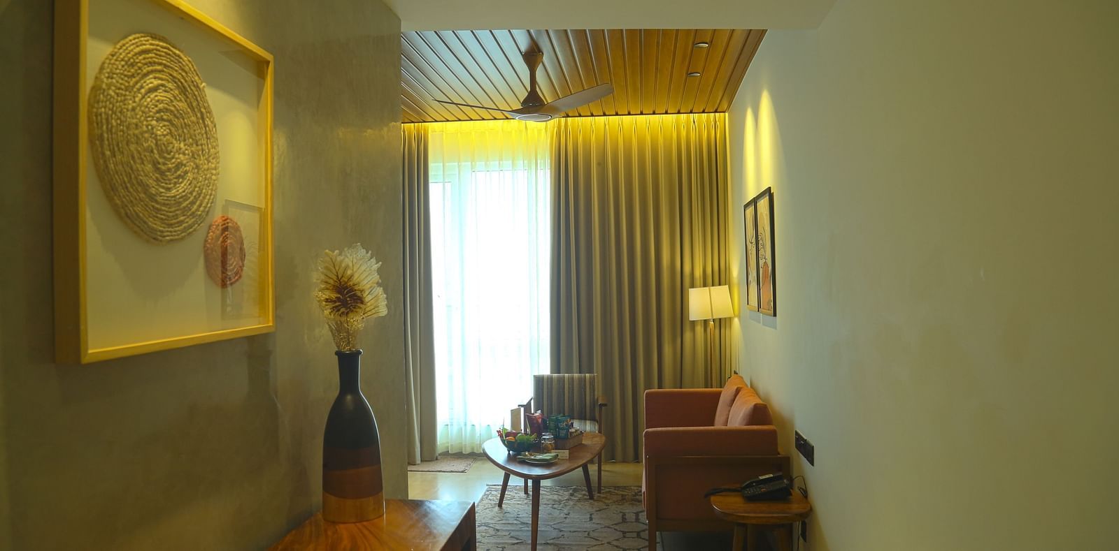 An image of the living area of the pent house with wall hangings, cupboards, sofa, table, and bright lighting - Great Trails Yercaud by GRT Hotels 