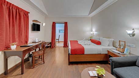A bedroom at Holiday Home Resort, Kodaikanal, featuring a bed,  a wooden desk and a chair, and a sofa with a coffee table in the foreground. 