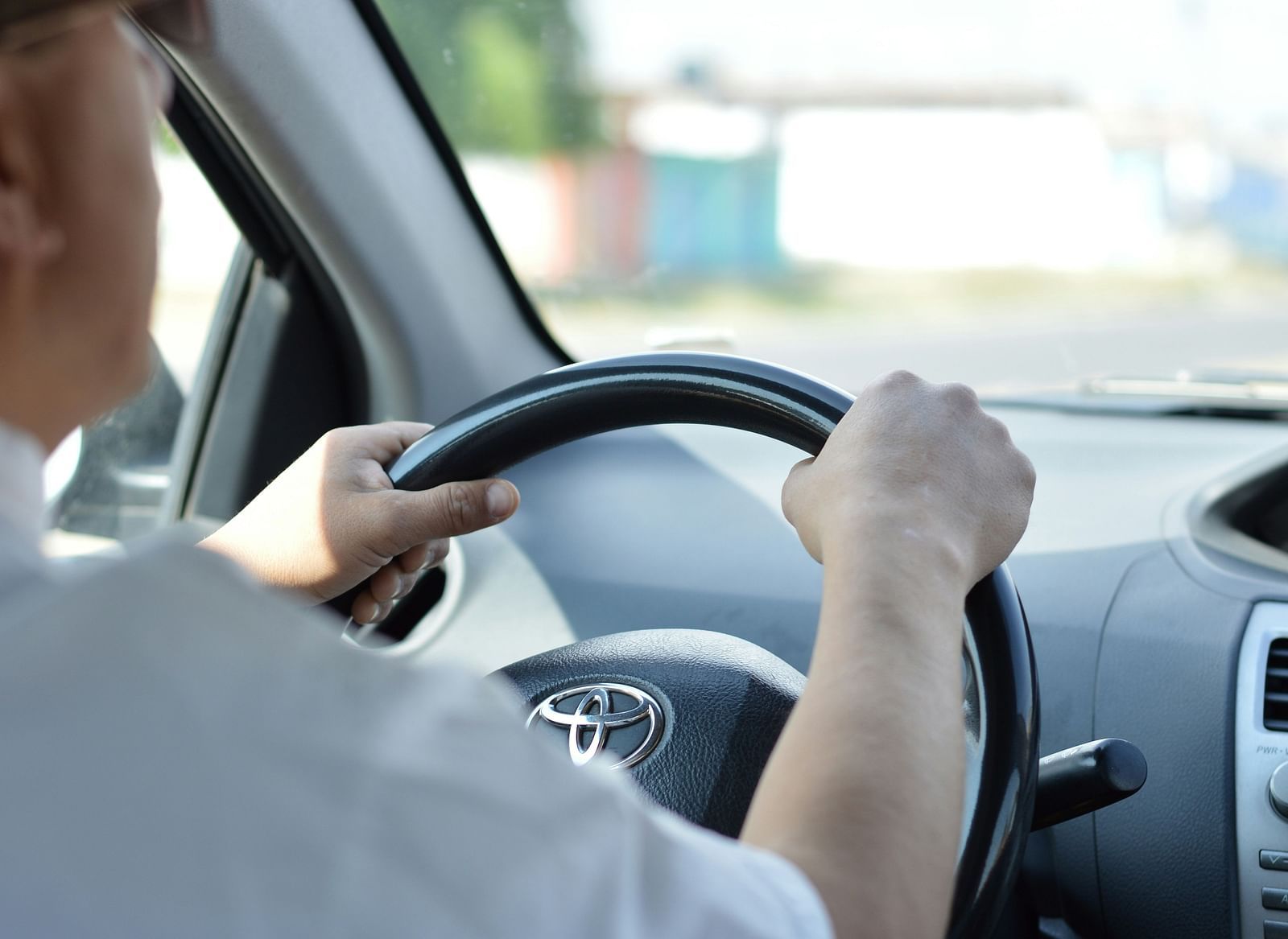 A person driving a car with a Toyota logo on the steering wheel.