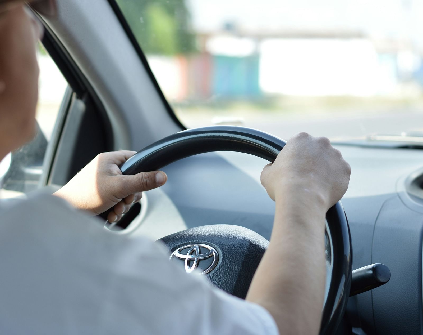 Close-up of a person's hands on a car steering wheel while driving.
