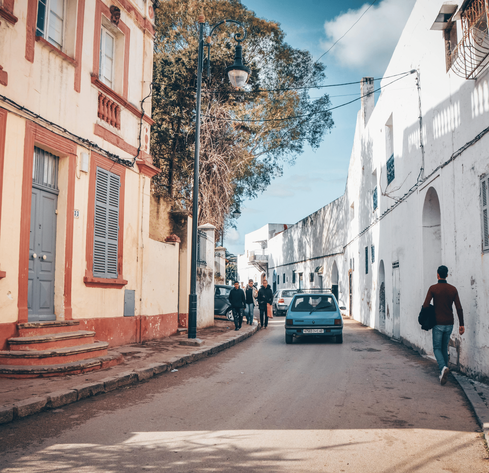 A narrow, winding street is lined with colourful buildings under a blue sky.