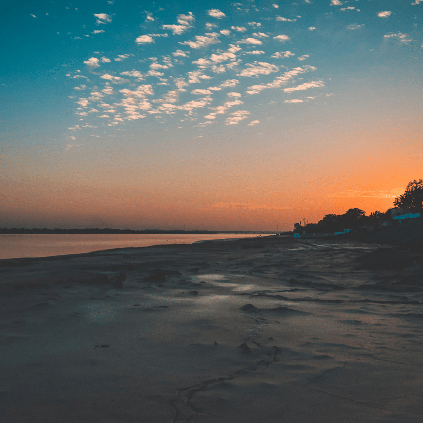 An overview of a beach in Bharuch during the sunset with orange-blue sky, white clouds, and the Arabian Sea in view. This is the mid-stop on your Narmada Parikrama by Bus tour.