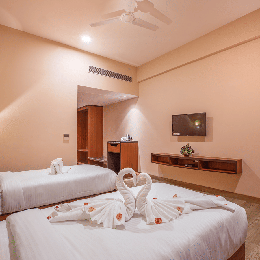 A modern bedroom at The Lalita Grand Mathura - Vrindavan featuring twin beds, swan towel art on white bedding, a wall-mounted TV, and ambient lighting.