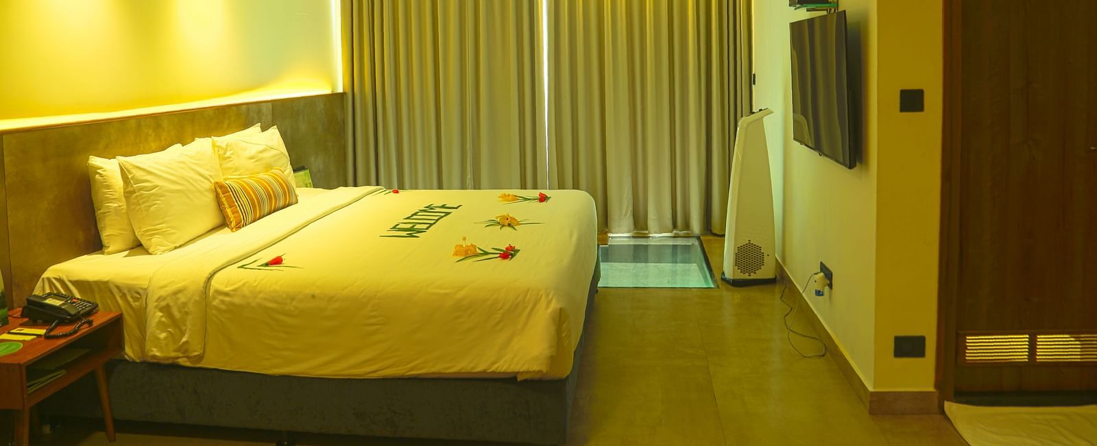 An image of a panorama view room with a king size bed, bed size table, flat screen TV with the curtains closed - Great Trails Yercaud by GRT Hotels