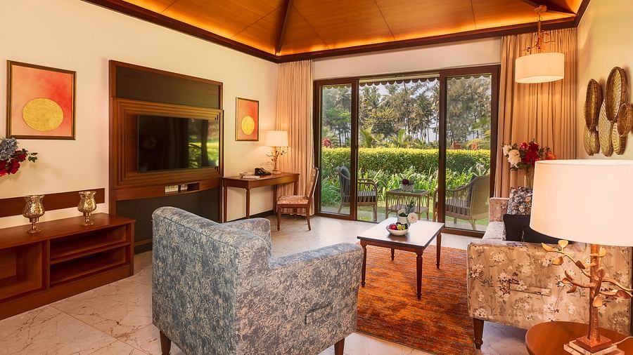 Gamyam Retreat, Kumta - The living area with sofas and television and a ceiling to door window opening to a garden
