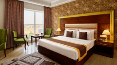 a double bed, nightstand with a lamp on it, and armchairs beside a coffee table in the SUPER DELUXE ROOM - Royal Kingdom Sarovar Portico, Pilibhit