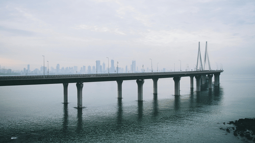 A long sea bridge extending across the water with city skyline faintly visible in the background.