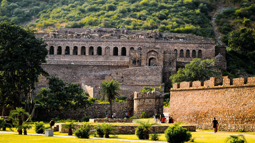 A stone fort with multiple arched openings, surrounded by trees and a green field.