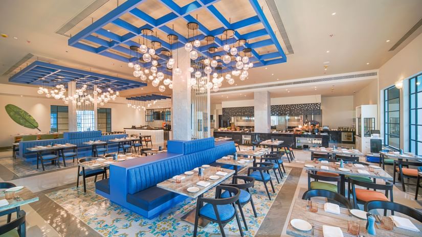 A colourful and modern restaurant interior with blue seating, patterned floor tiles, and an elaborate ceiling light fixture | SPR Kitchen | Sarovar Portico, Sriperumbudur