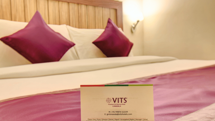 Close-up of king-size bed with purple cushions and welcome card at VITS Lonavala.