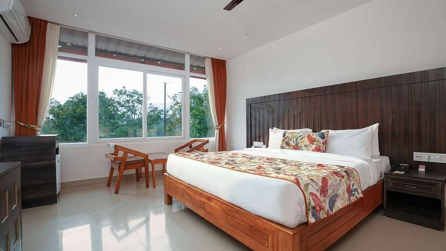 Deluxe room featuring large windows with a nature view, a spacious bed, air conditioning, wooden storage units, and a television at Summit Green Lake Tea Resort & Spa, Kaziranga5