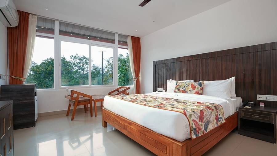 Deluxe room featuring large windows with a nature view, a spacious bed, air conditioning, wooden storage units, and a television at Summit Green Lake Tea Resort & Spa, Kaziranga5