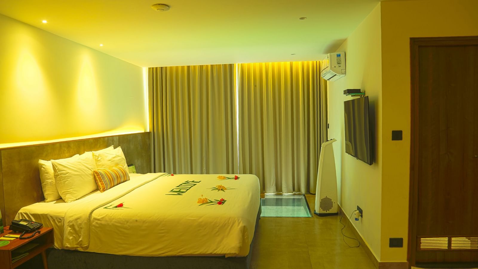 An image of a panorama view room with a king size bed, bed size table, flat screen TV with the curtains closed - Great Trails Yercaud by GRT Hotels