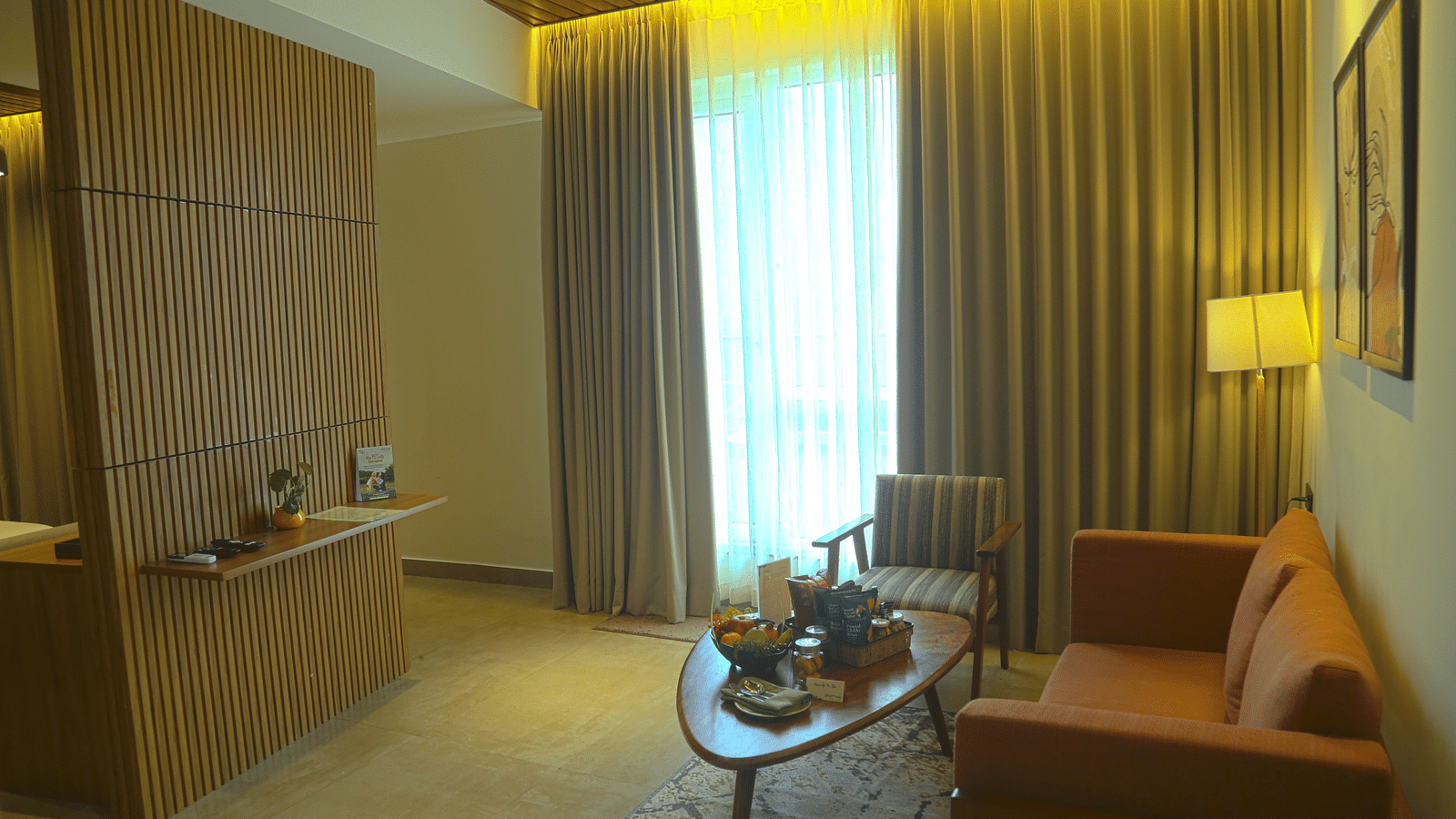 An image of the separate living area of the pent house with sofa set, a table, lamp, wall hangings, and an expansive window - Great Trails Yercaud by GRT Hotels