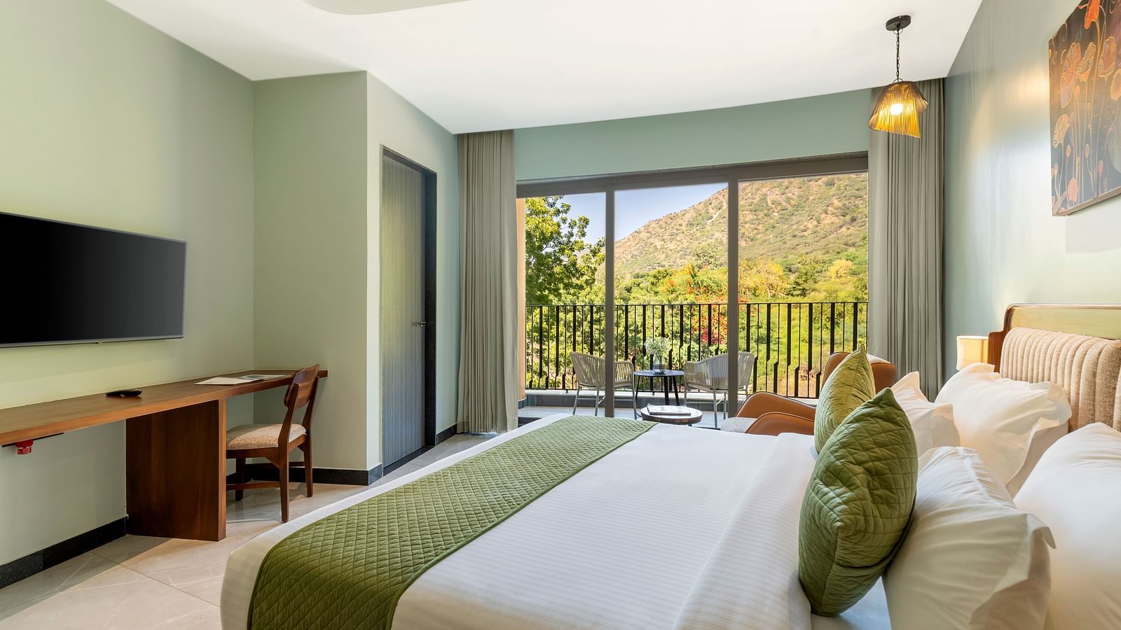 Club Suite with Valley View Sitout showcasing a king size bed with green and white linens, a work desk, and a balcony with a scenic view at The Qualia Resort Club & Brewery, Udaipur.