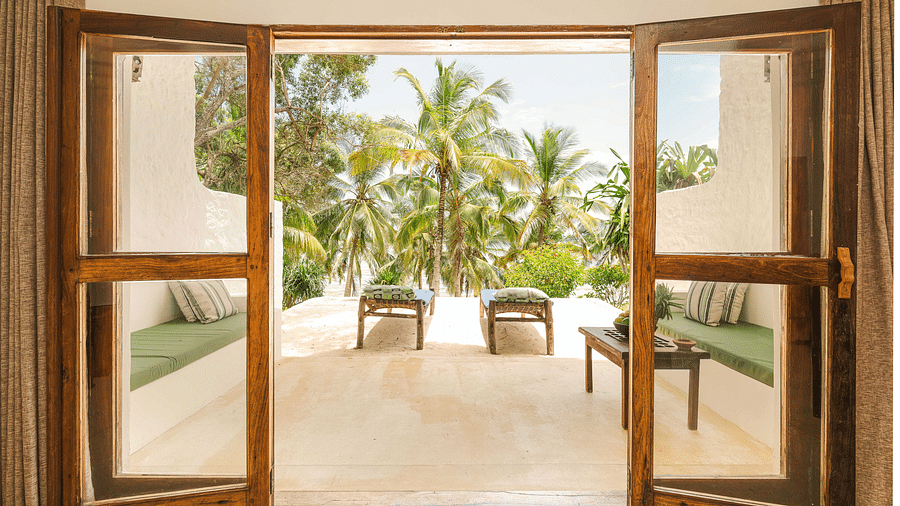 Open wooden doors leading to a outside patio area with a view of palm trees and the ocean beyond - Shooting Star Boutique Hotel. 