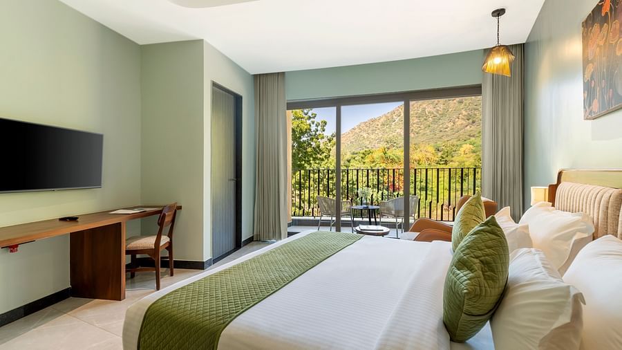 Club Suite with Valley View Sitout showcasing a king size bed with green and white linens, a work desk, and a balcony with a scenic view at The Qualia Resort Club & Brewery, Udaipur.