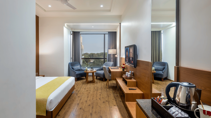 A premium room in Lords Inn Somnath with modern interiors, featuring a well furnished space with lounge chairs, entertainment unit and a large window offering a view of the outdoors.