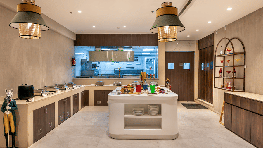 A buffet counter area with in the Blue Coriander restaurant featuring sleek white counters, stylish light fixtures, and decor – Skkylight Lords Inn, Nanded