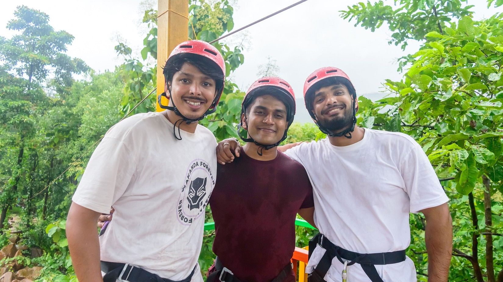 3 friends standing side by side happily, while wearing helmets and safety harnesses.