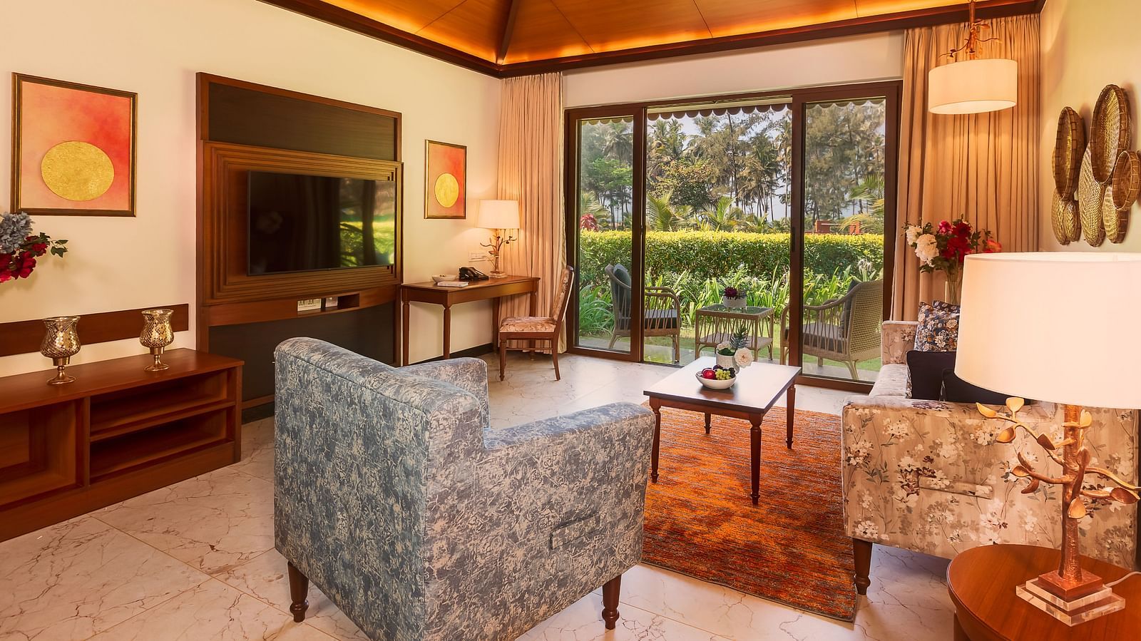 Gamyam Retreat, Kumta - The living area with sofas and television and a ceiling to door window opening to a garden