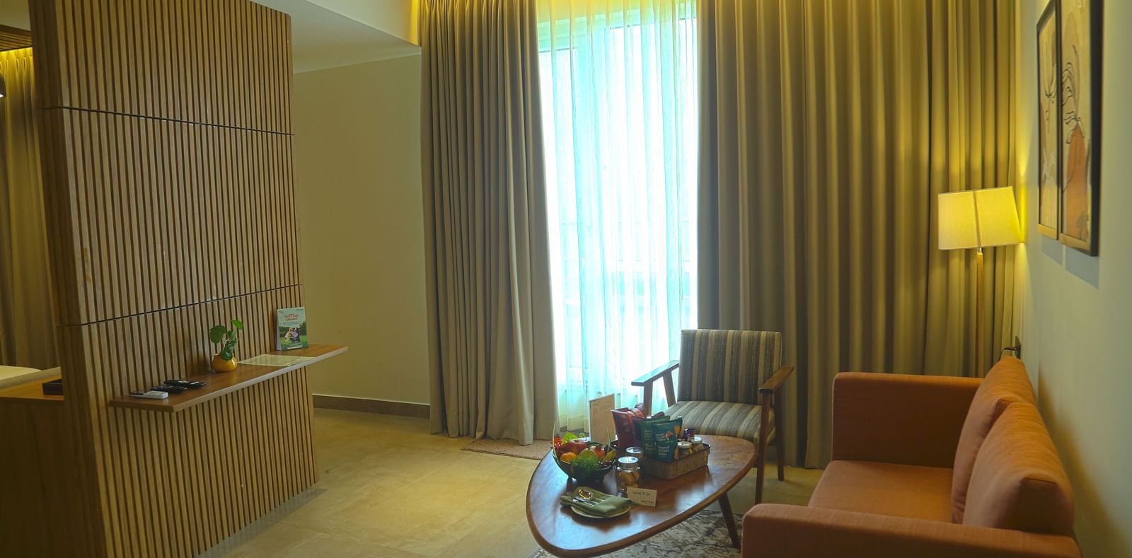 An image of the separate living area of the pent house with sofa set, a table, lamp, wall hangings, and an expansive window - Great Trails Yercaud by GRT Hotels