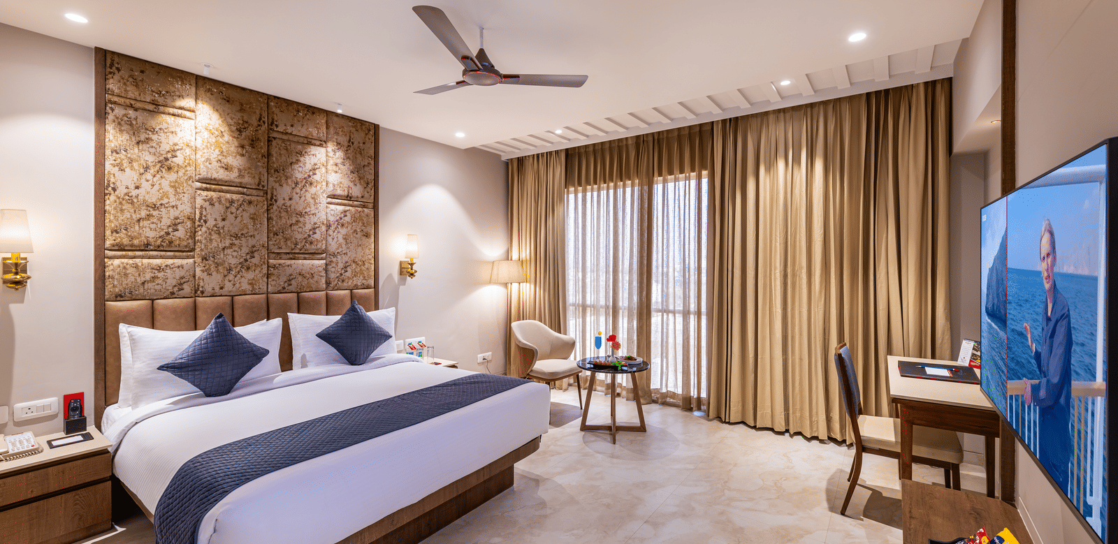 A well-lit Deluxe Room featuring a king size bed, warm wooden accents, and a large window with neutral-toned curtains – Skkylight Lords Inn, Nanded