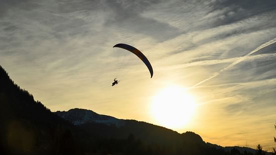 A person paragliding with a sun set behind him