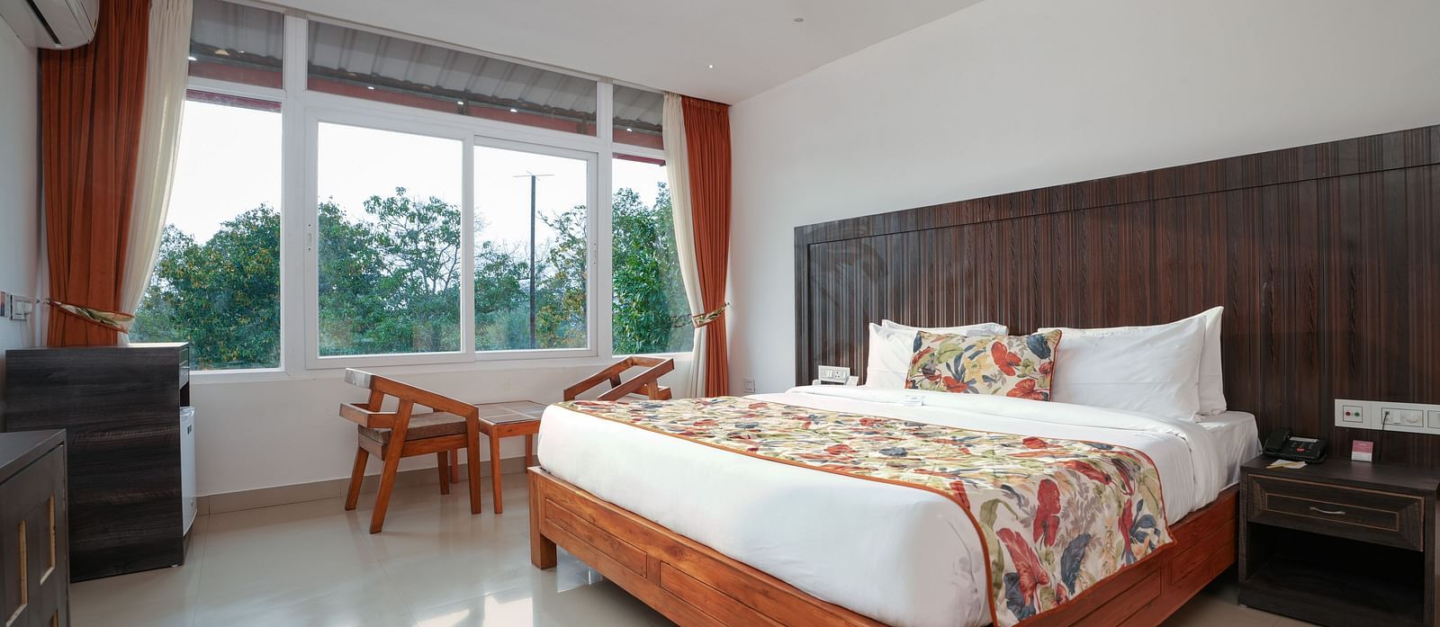 Deluxe room featuring large windows with a nature view, a spacious bed, air conditioning, wooden storage units, and a television at Summit Green Lake Tea Resort & Spa, Kaziranga5
