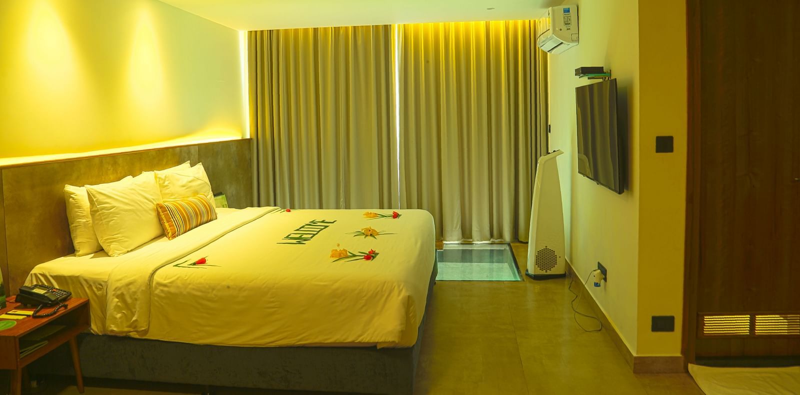 An image of a panorama view room with a king size bed, bed size table, flat screen TV with the curtains closed - Great Trails Yercaud by GRT Hotels