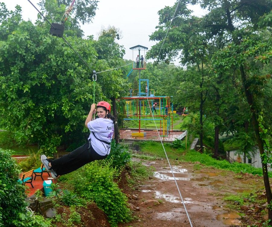alt-text A girl with a helmet with her legs up, ziplining on an adventure course, in the midst of a forest.