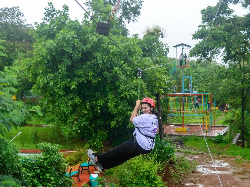 A girl with a helmet with her legs up, ziplining on an adventure course, in the midst of a forest.