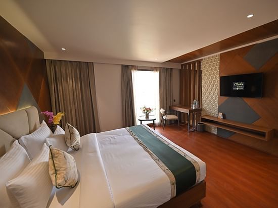 Side view of the bedroom featuring a wall-mounted television and a window with partially drawn curtains at Clarks Collection Grand Sapphire, Ajmer.