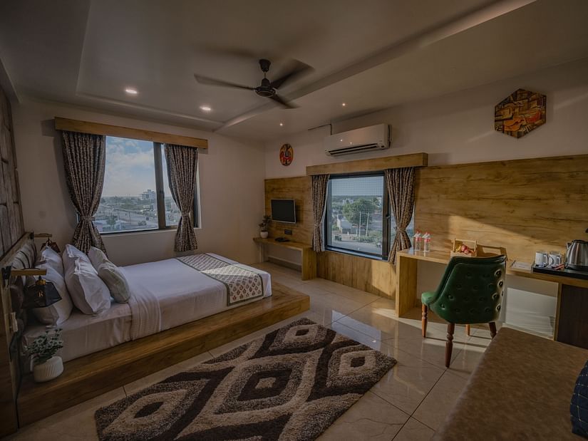 A bedroom at Clarks Collection Somnath featuring a double bed, two windows, ac, chair, study desk, wall-mounted TV, and fan.