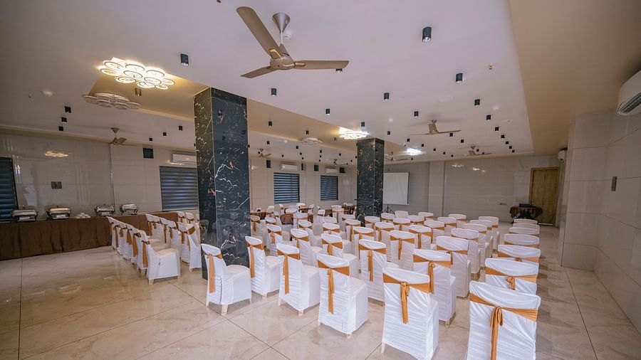 A hall with chairs around square tables, black pillars, and ceiling lights at Clarks Collection Somnath.