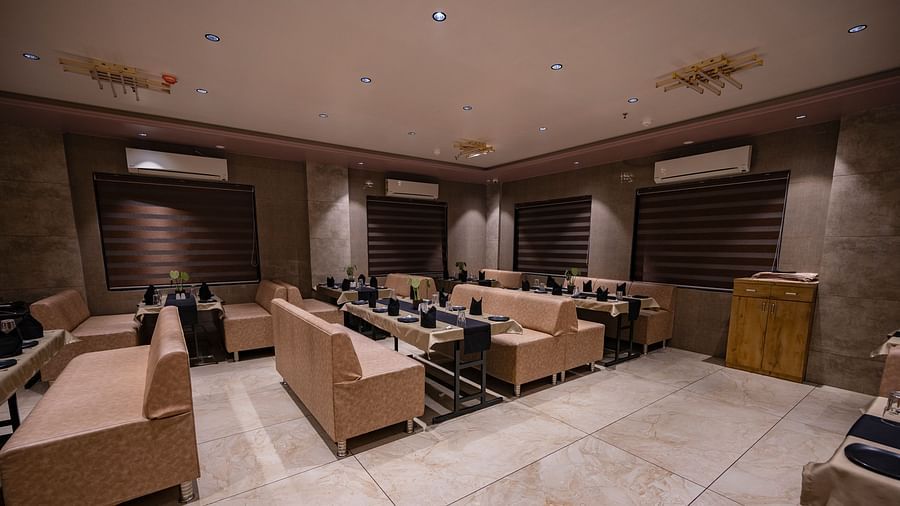 The lounge-style seating area with cushioned arm sofas, tables wit neatly arranged plates, spoon, glass and elegant lighting at Clarks Collection Somnath.