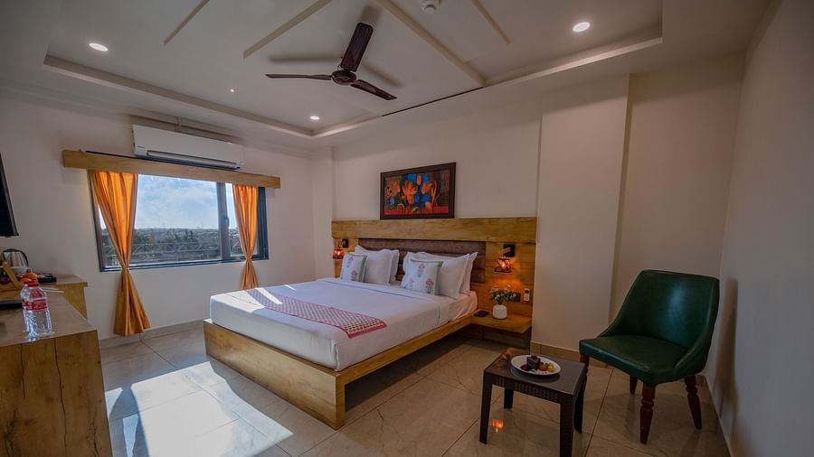A room with double bed, green chairs, frame art work, and large window at Clarks Collection, Somnath.