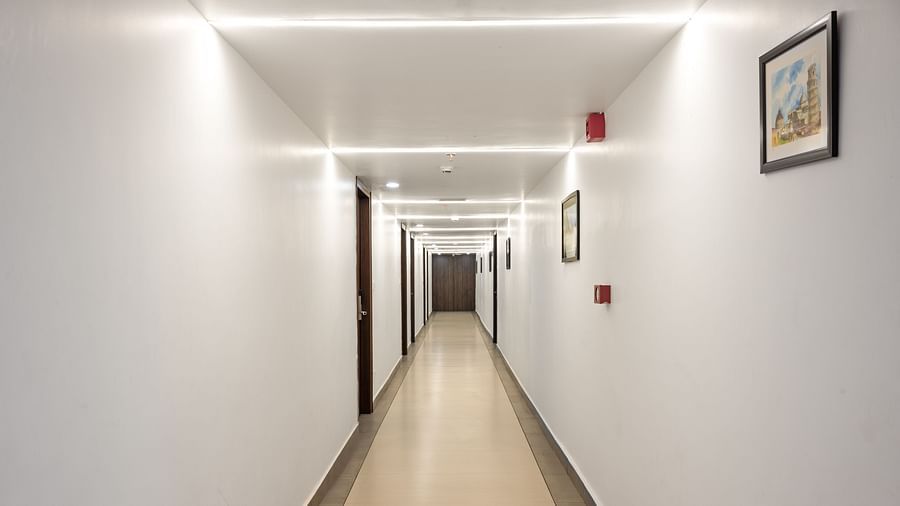 A long, well-lit hotel corridor with  walls, framed artwork, and multiple doors on both sides. - Clarks Inn Express, Near Jammu Bari Brahmana Railway Station.