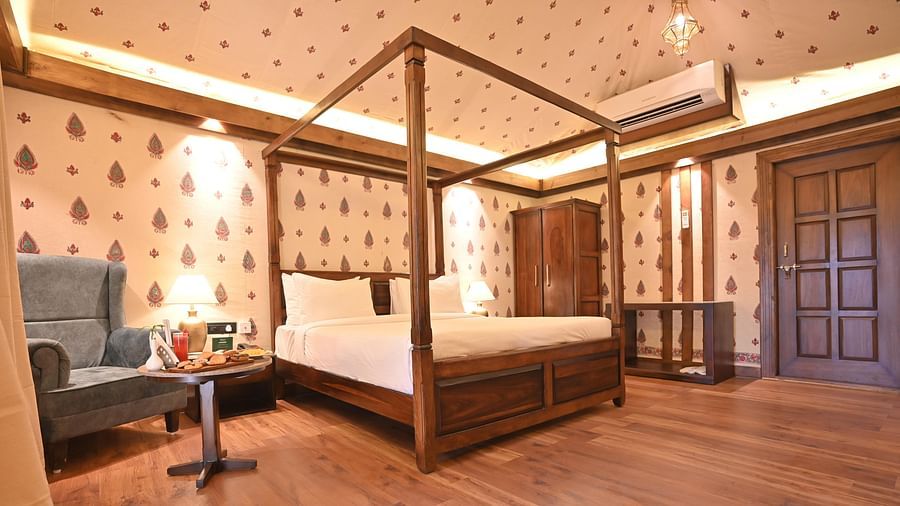 A Premium Tent featuring a poster bed, air conditioner, wardrobe, bedside table with lamp, and a sofa chair with centre table where food items are kept - The Baagh Ananta Elite, Ranthambore