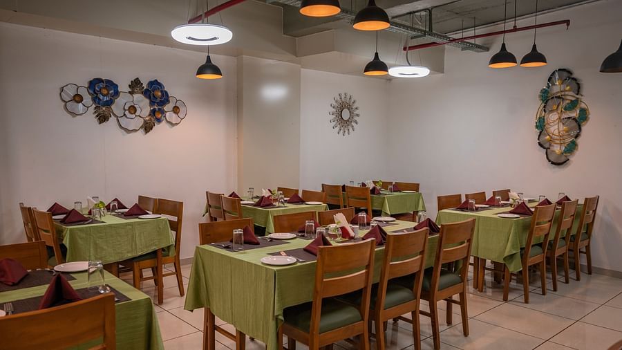 Clarks Safari Kheda's dining area with multiple tables are set with neat coverings and chairs, lights, neatly arranged tissues, plates, spoons, a small money plant on the centre and decorative elements on the walls.